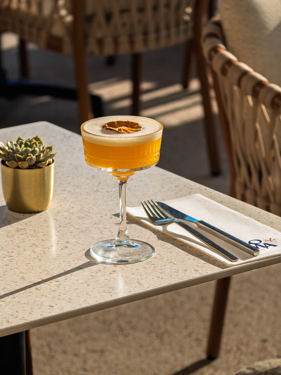 An amber cocktail in a coupe, dried citrus, on a napkin embroidered with Loma