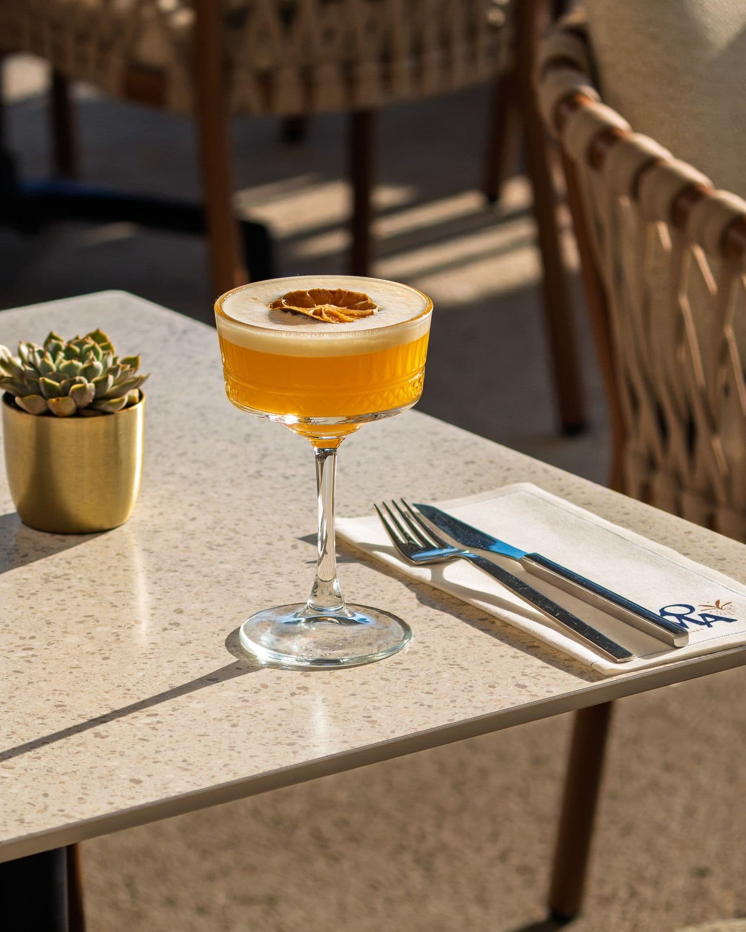 Cocktail ambré au soleil sur la terrasse du Loma, à côté d’une serviette brodée au logo