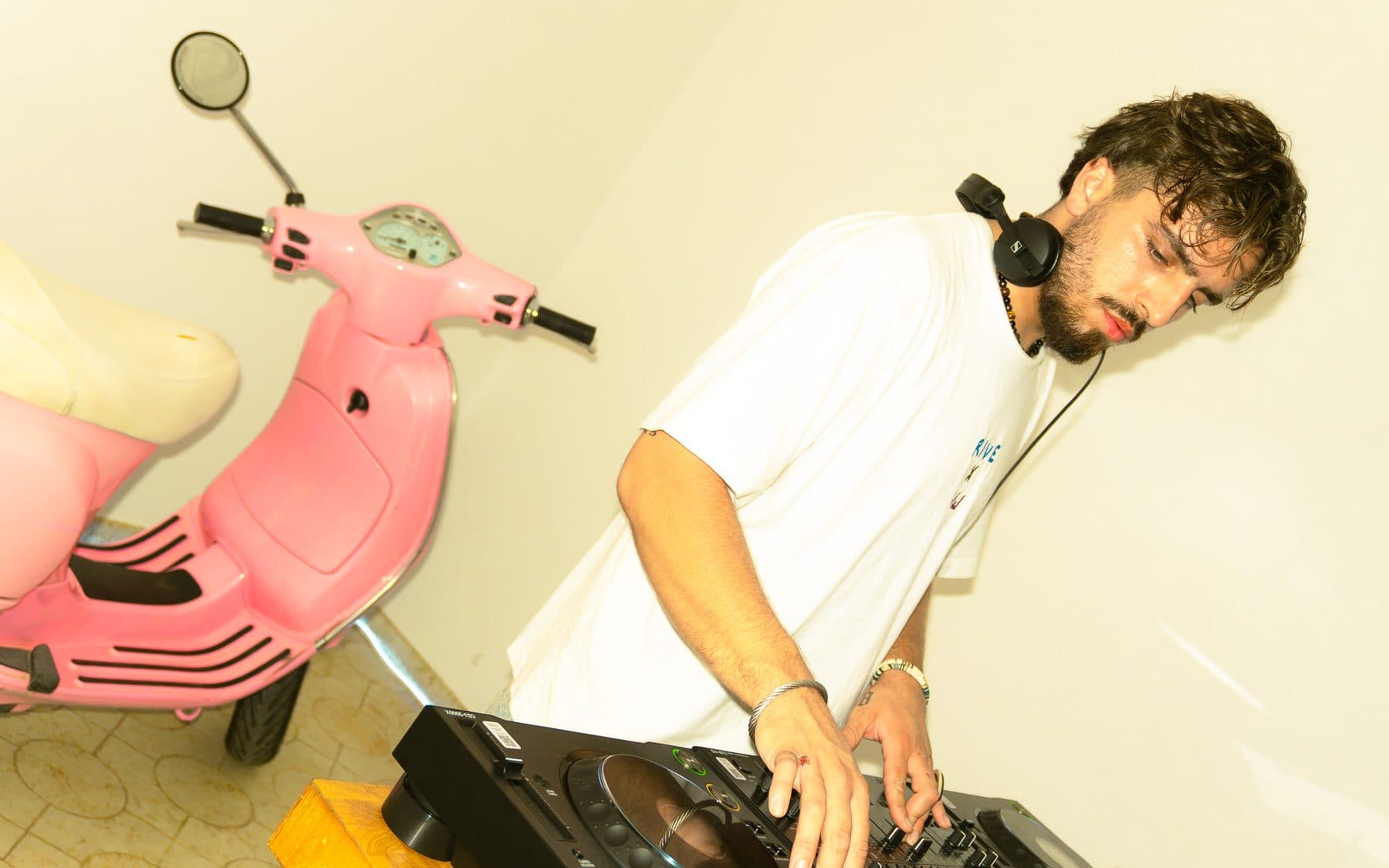 Logan What at the decks, headphones around his neck, a pink scooter beside him