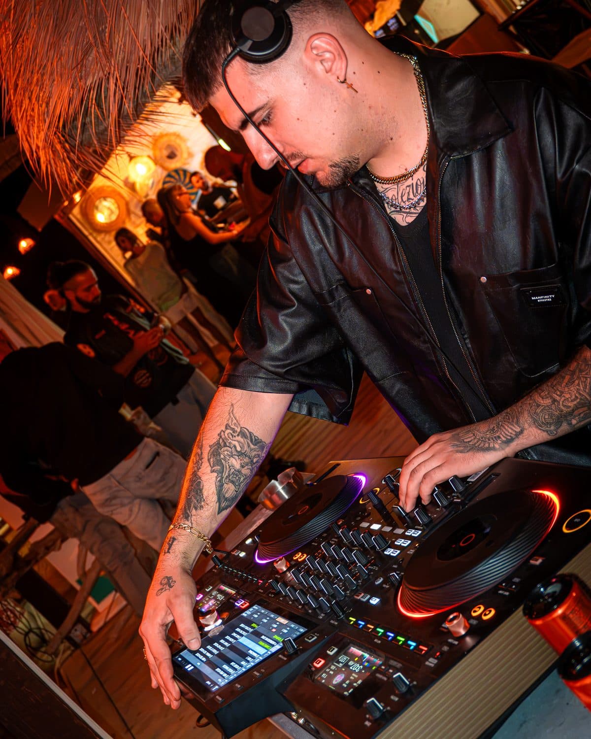 Hands on the decks at night, headphones on, orange lights in the background